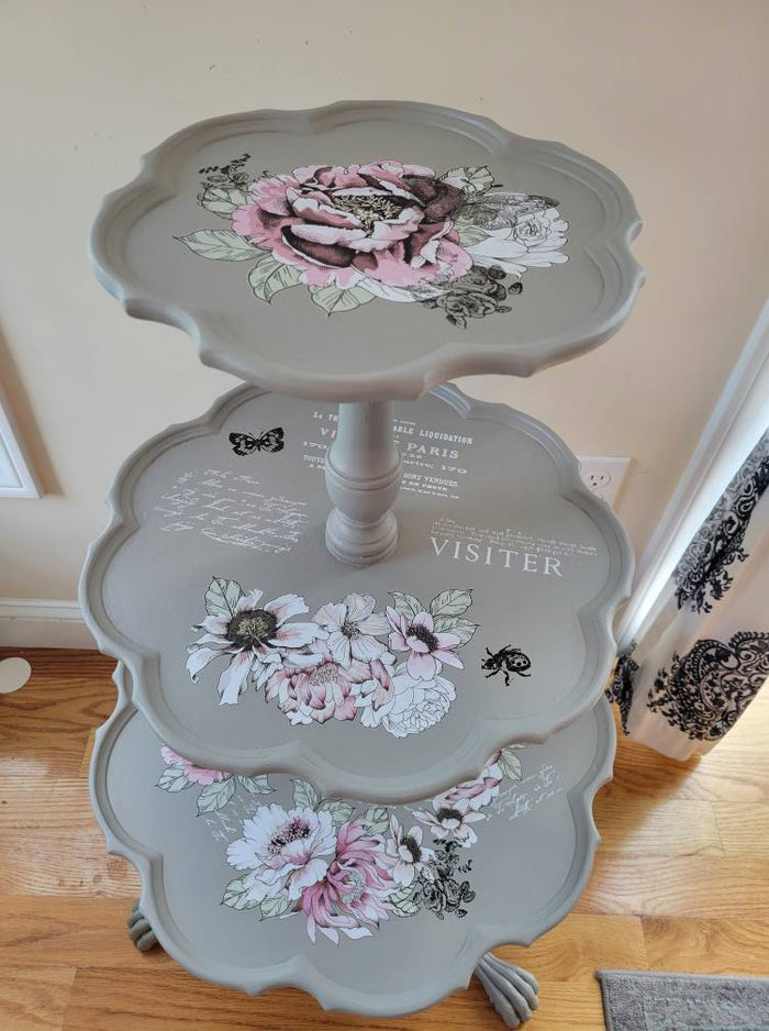 A vintage three-tier pie table with floral motif decorations in shades of pink and white, and the words 'VISITOR' painted on the middle tier.