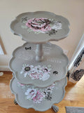A vintage three-tier pie table with floral motif decorations in shades of pink and white, and the words 'VISITOR' painted on the middle tier.