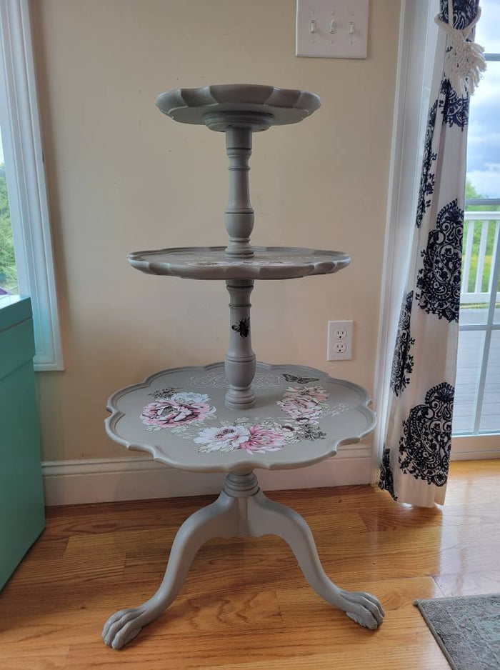 Three tiered light gray table against cream wall sitting on wood floor