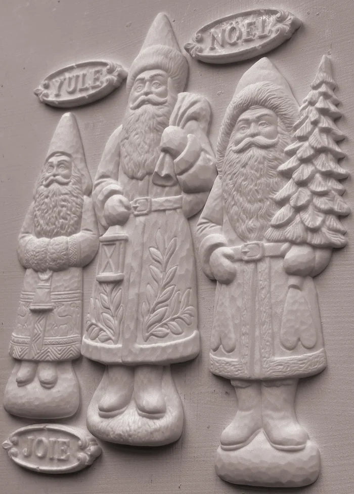Three carved Santa Claus figures in a relief style, labeled Yule, Noel, and Joy, on a textured gray background.