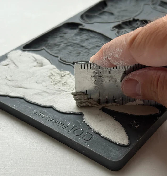 Hand using a ruler to measure a silicone mold with white material on a light background