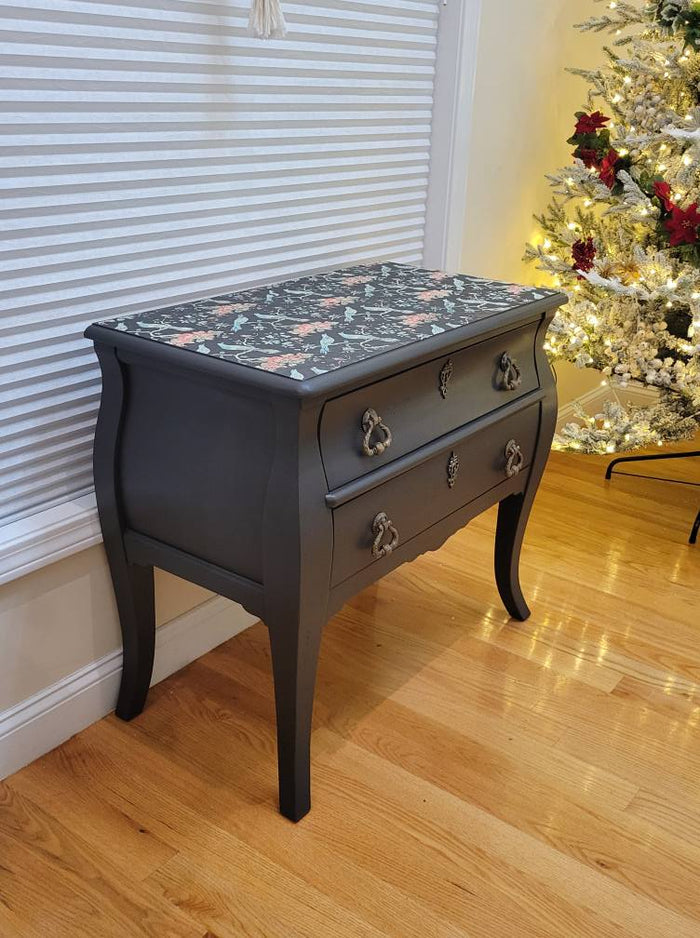 A Bombay style chest of drawers with a floral pattern on the top, antique black finish, and metal handles.