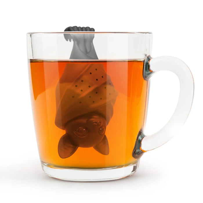 A clear glass mug filled with tea, featuring a bat-shaped tea infuser hanging inside the cup on a white background.