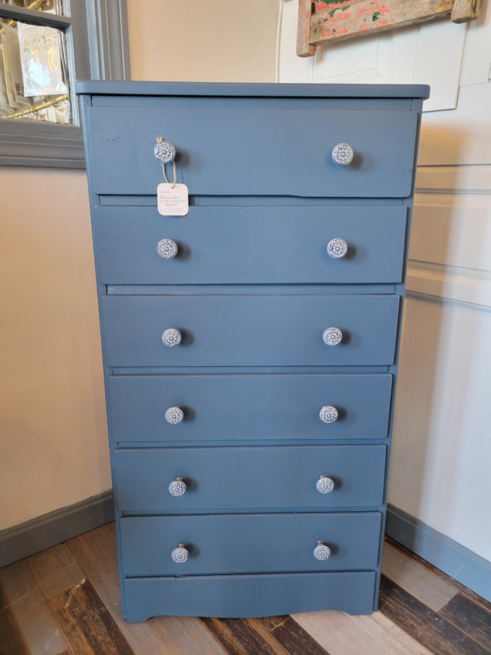 A blue dresser with six drawers, positioned against a wall in a home setting
