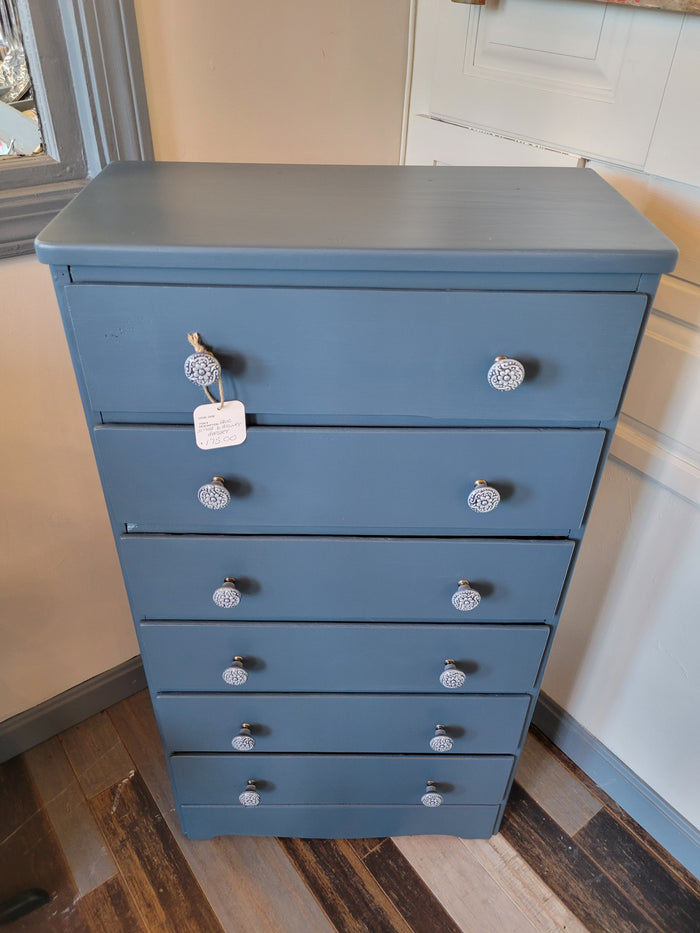 A blue dresser with six drawers, positioned against a wall in a home setting