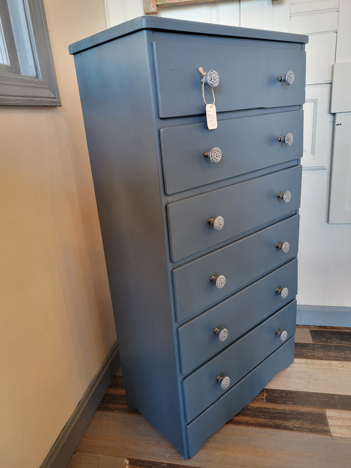 A blue dresser with six drawers, positioned against a wall in a home setting