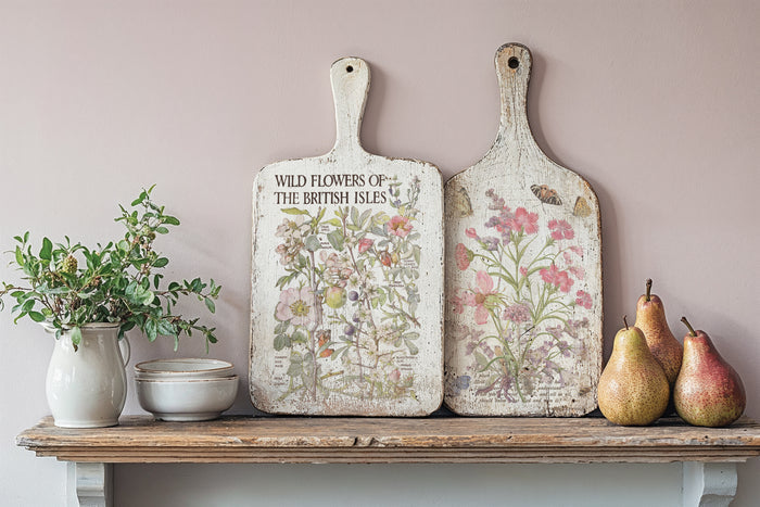Decorative cutting boards with floral designs on a shelf against a light pink wall.