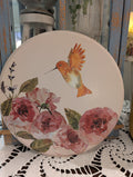 Decorative plate with a hummingbird and floral design on a doily.